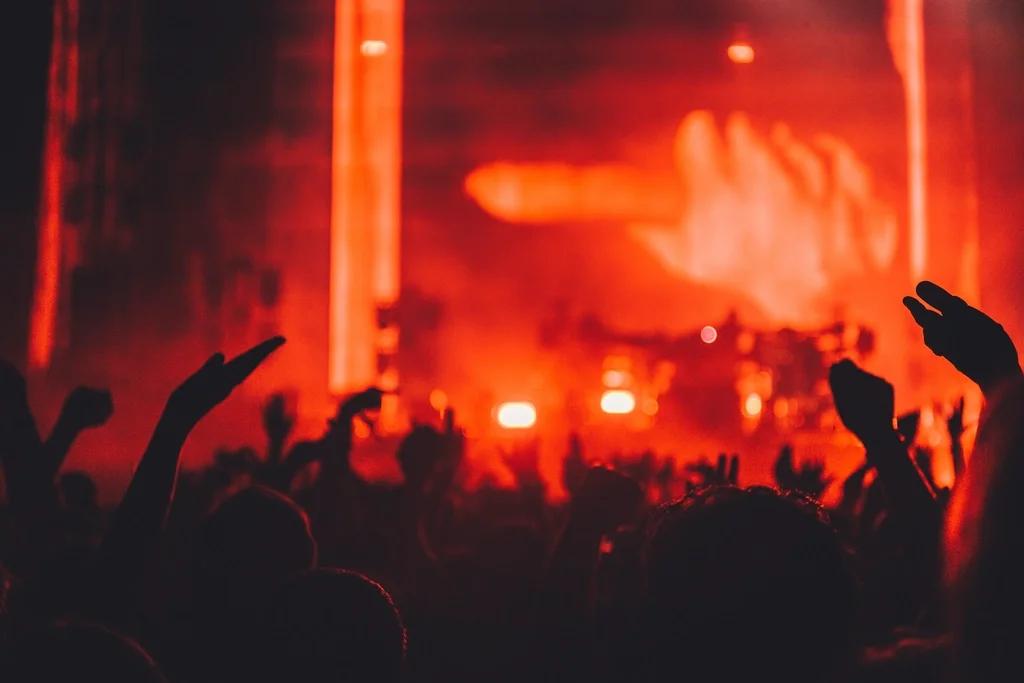 A packed crowd with hands up under red stage lights at a live hip-hop show